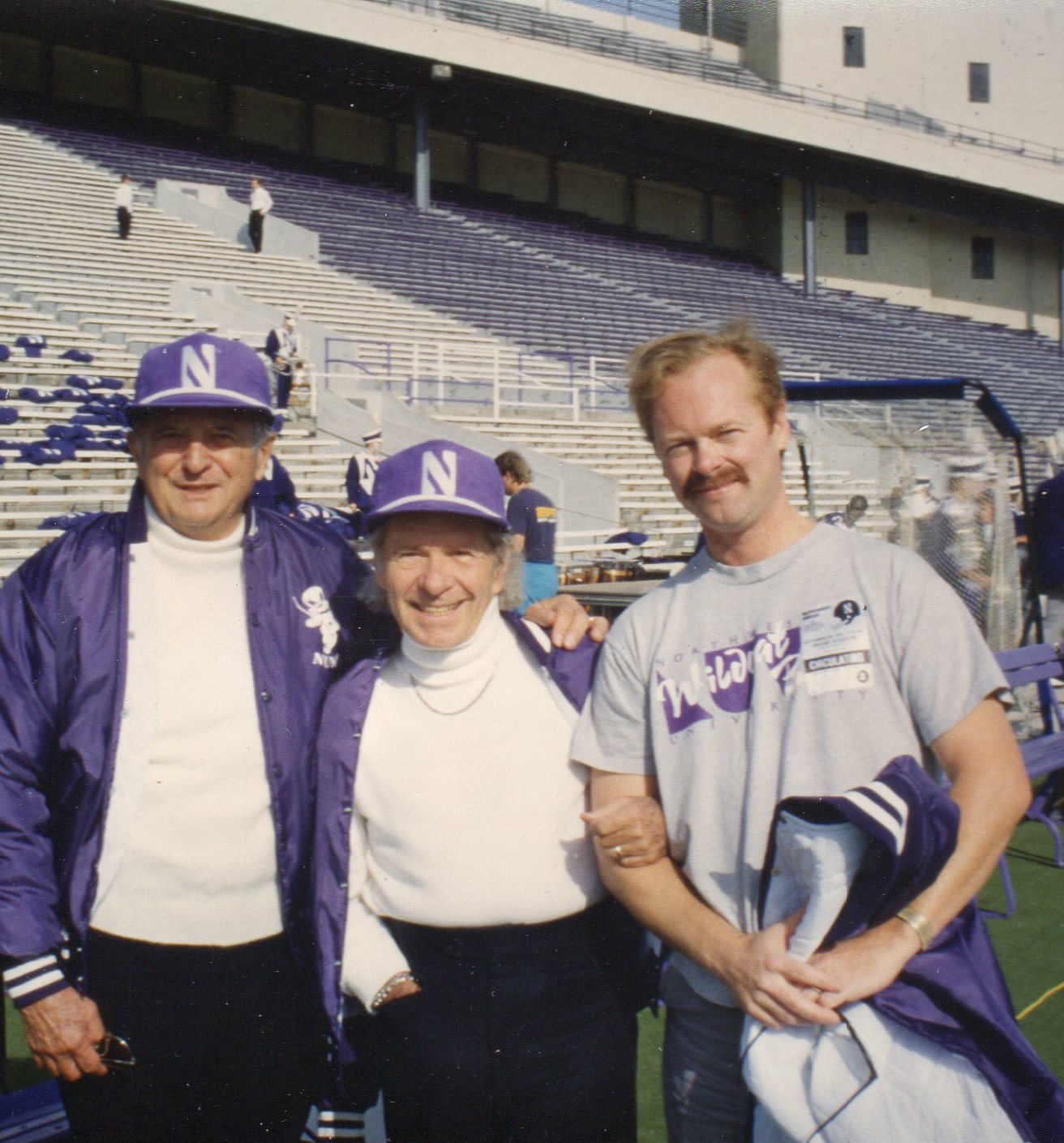 Bill Ludwig, Fred Fennell, and Christopher Morris at Northwestern University, standing together and wearing Northeastern hats, jackets, and shirts.